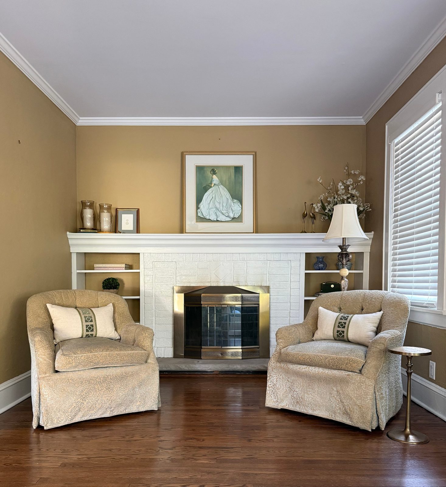 The restyled living room — two chairs and a small table facing the fireplace, with the original built-ins styled lightly on either side. Oradell Colonial.